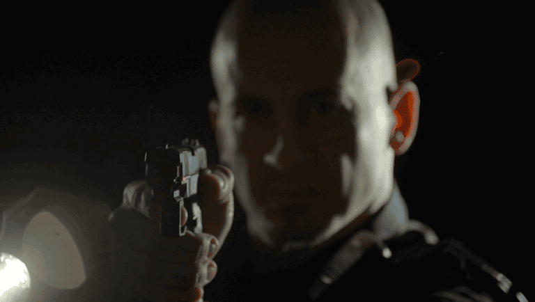 Suspenseful man aiming gun in dark scene, dramatic lighting.
